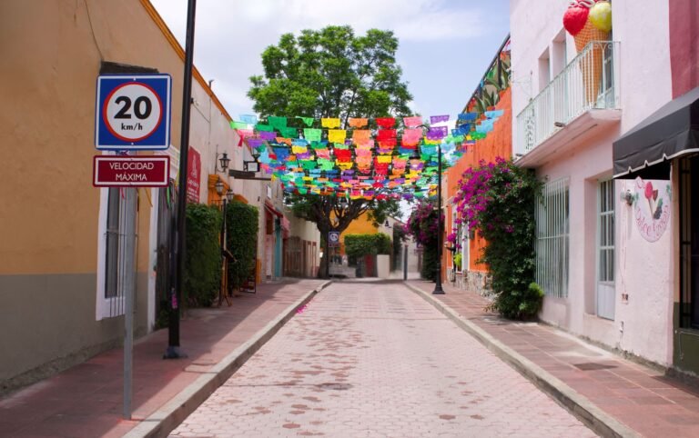Calle adoquinada de un pueblo mexicano con papel picado de colores colgado entre las casas