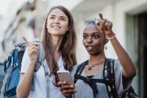 Dos viajeras con mochila consultando el móvil para orientarse en una ciudad